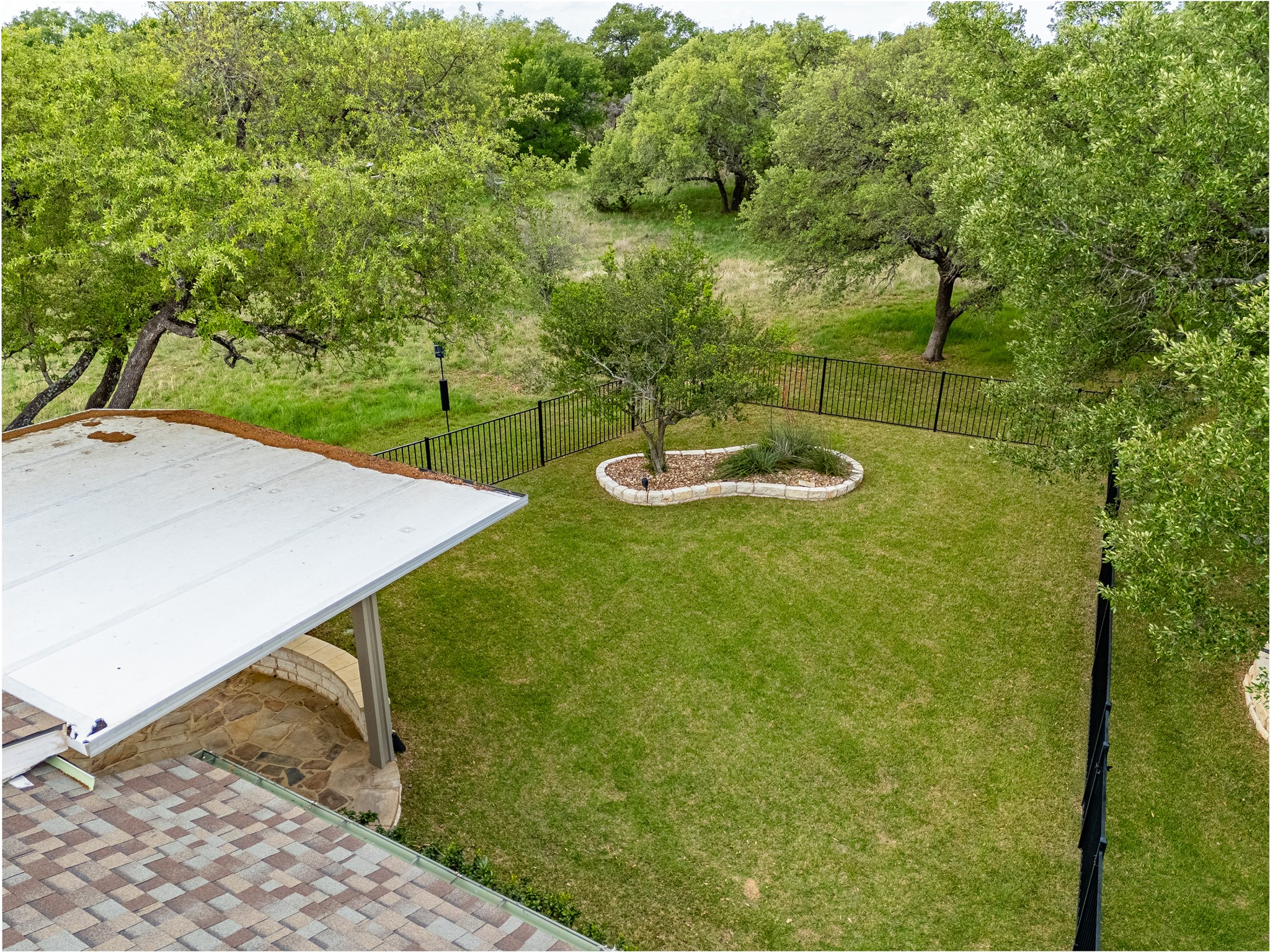 214 Summit Street Georgetown, TX 78633 - Photo 33 of 38 The property features an extensive lawn area, a black metal fence, and a stone-edged planting bed with a tree and shrubs