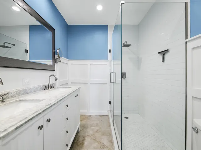 a bathroom with a granite countertop sink two mirror and shower