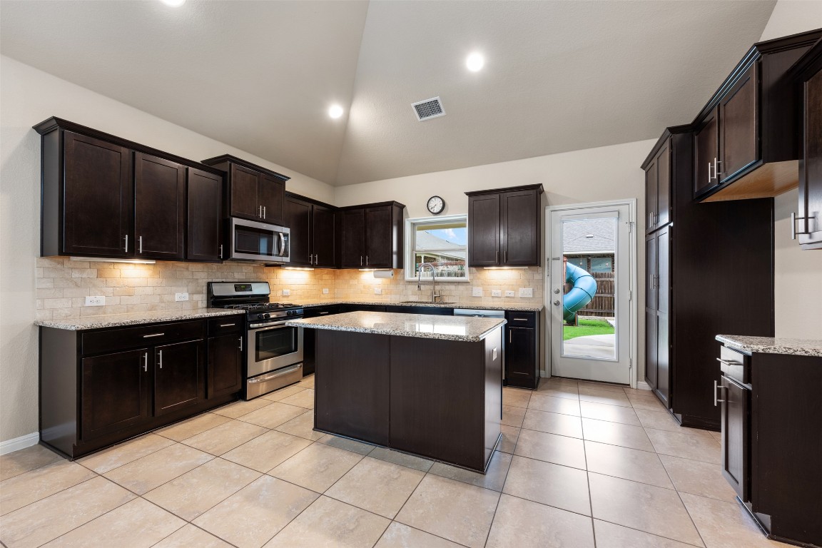 533 Flag Lane Leander, TX 78641 - Photo 11 of 40 Kitchen featuring appliances with stainless steel finishes, a sink, tasteful backsplash, light stone counters, and a kitchen island