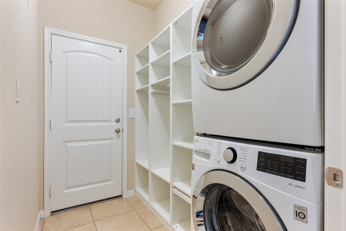 533 Flag Lane Leander, TX 78641 - Photo 23 of 40 Laundry area with stacked washing machine and dryer, light tile flooring, and cubby storage with door to garage.