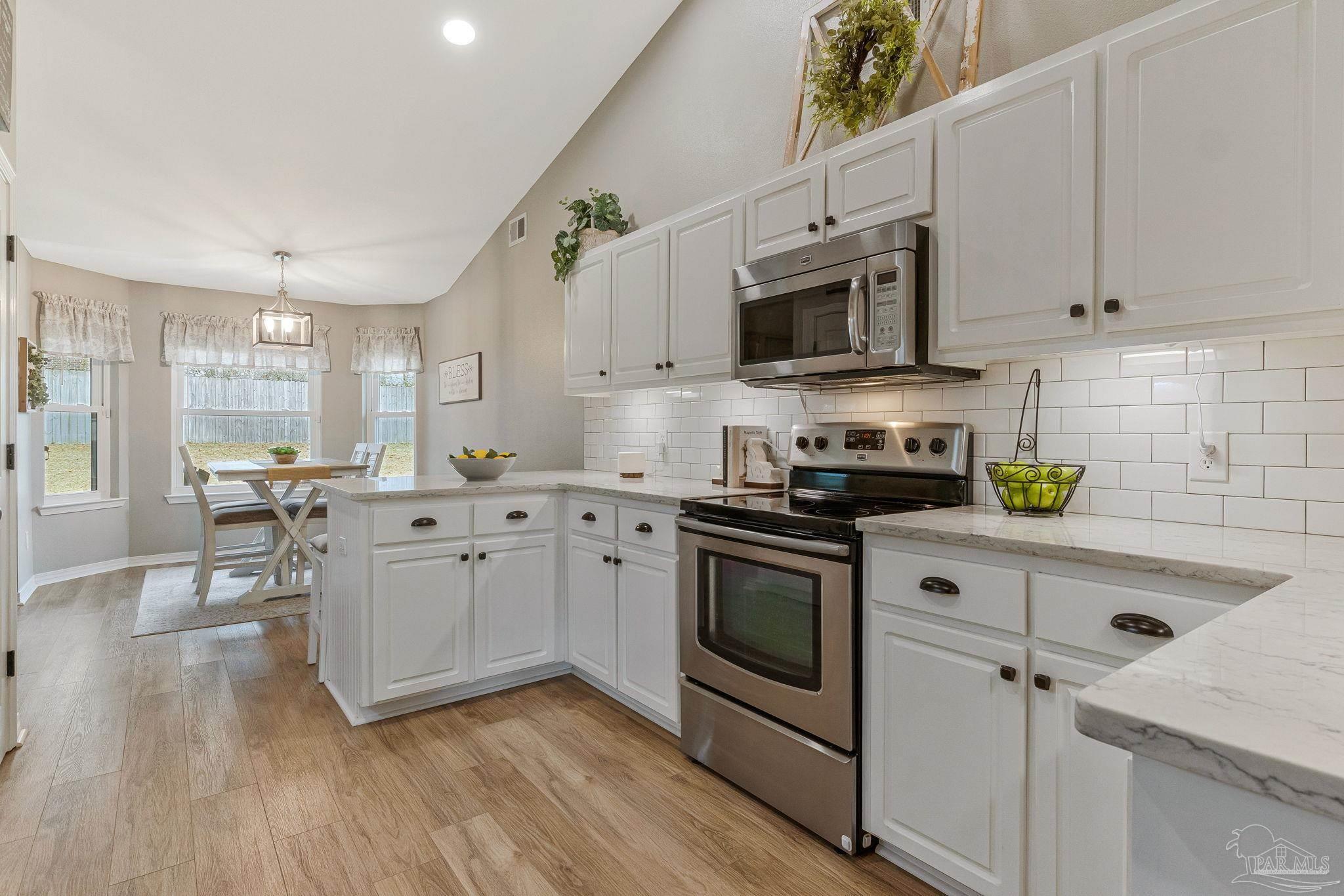 2407 Pine Forest Road Cantonment, FL 32533 - Photo 11 of 60 a kitchen with stainless steel appliances white cabinets a sink a stove a microwave and wooden floors