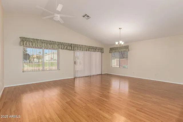an empty room with wooden floor chandelier and windows