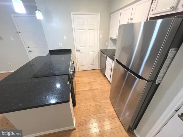 a view of a refrigerator in kitchen and an empty room with wooden floor