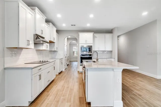 a kitchen with stainless steel appliances granite countertop a stove top oven a sink a refrigerator and white cabinets with wooden floor