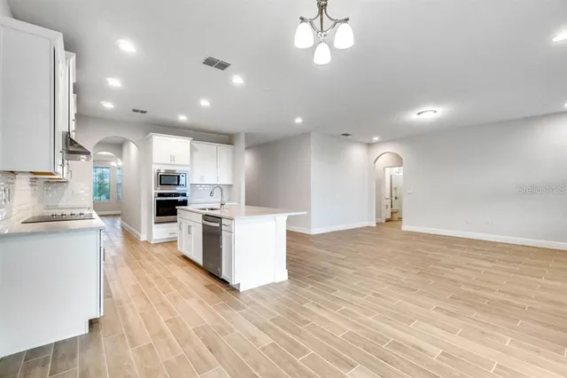 a kitchen with stainless steel appliances kitchen island granite countertop a stove top oven a sink a refrigerator and white cabinets