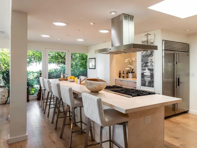a kitchen with stainless steel appliances kitchen island granite countertop a stove a refrigerator a sink a dining table and chairs with wooden floor