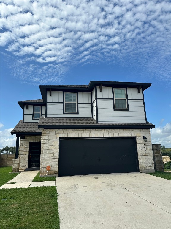 View of front facade with stone siding, concrete driveway, and an attached garage