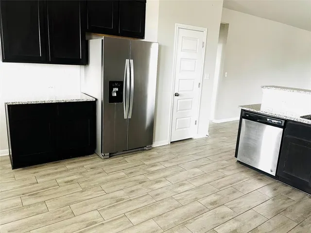 a view of a refrigerator in kitchen and an empty room with wooden floor