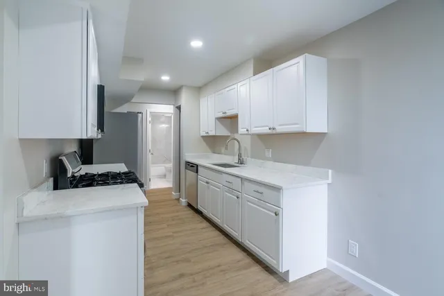 a kitchen with stainless steel appliances granite countertop a stove a sink a refrigerator white cabinets and wooden floor