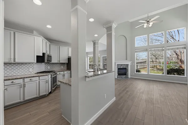 a large kitchen with stainless steel appliances granite countertop a stove a refrigerator a sink and white cabinets with wooden floor