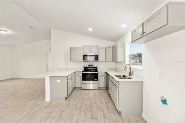 a kitchen with stainless steel appliances a stove top oven a sink a refrigerator white cabinets and wooden floor