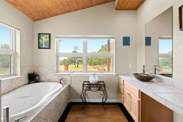 a bathroom with a granite countertop tub sink a window and mirror
