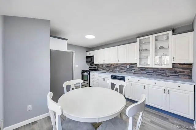 a kitchen with stainless steel appliances granite countertop a sink a stove a refrigerator with white cabinets and wooden floor