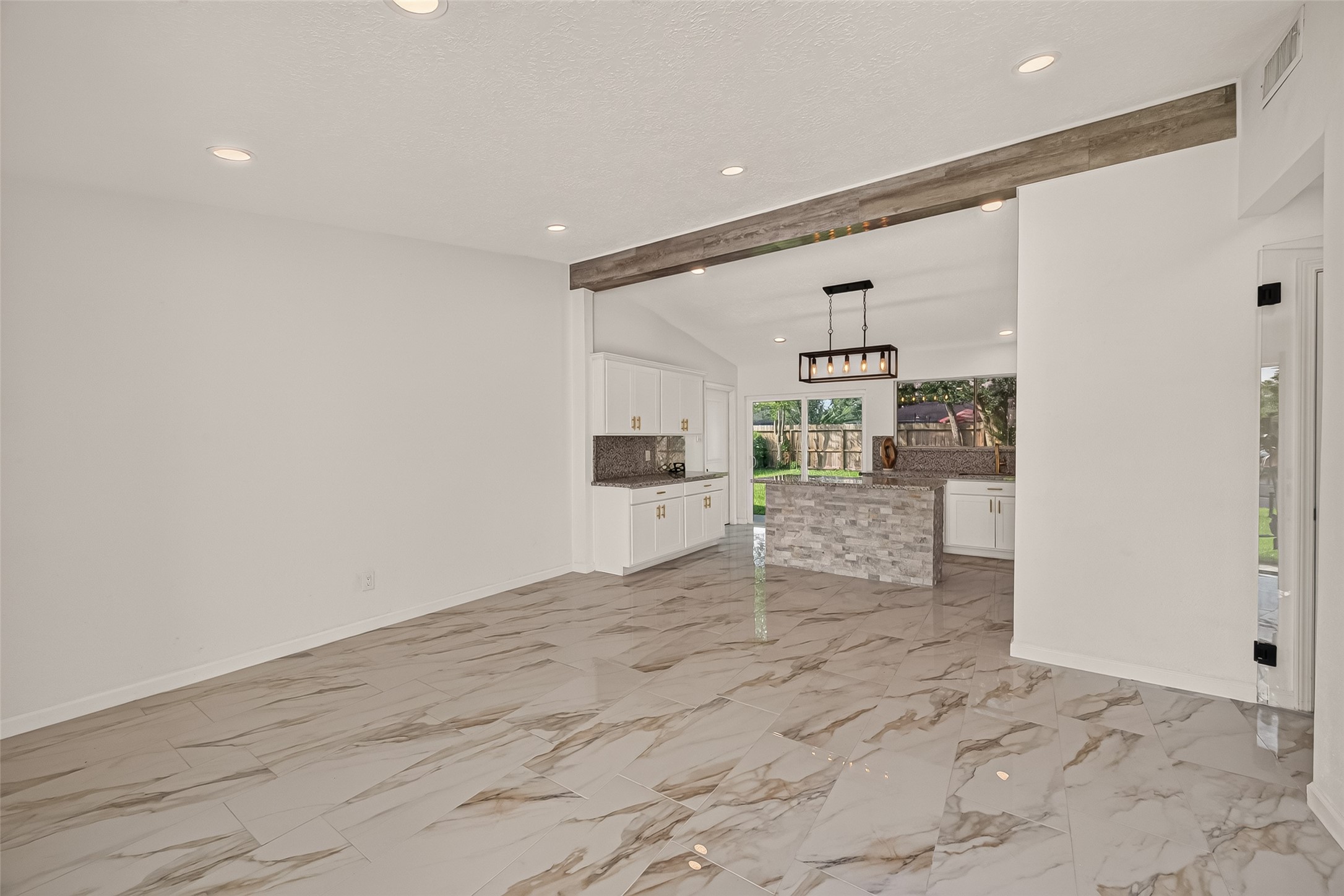16619 Tibet Road Friendswood, TX 77546 - Photo 6 of 29 This modern home features an open-concept layout with sleek, glossy marble floors and recessed lighting. The spacious kitchen boasts a central island with a stone finish, white cabinetry, and large windows offering plenty of natural light.
