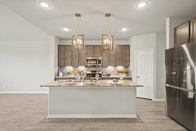 a kitchen with stainless steel appliances granite countertop a stove a sink a refrigerator and chairs