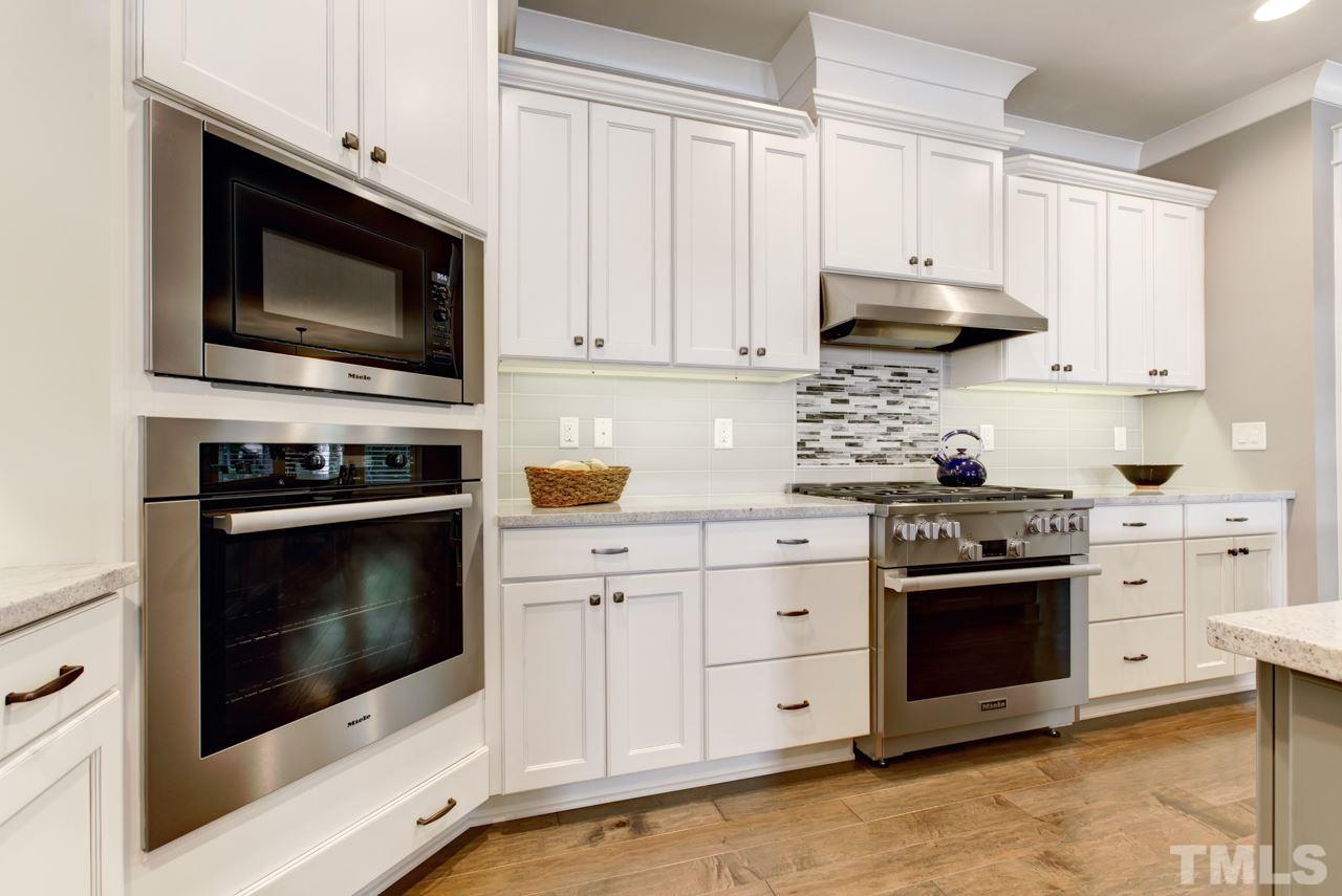1003 Collins Drive Raleigh, NC 27609 - Photo 6 of 25 Continue into the gourmet kitchen that offers Miele stainless steel appliances, granite counters, a huge center island with seating, cabinets with crown and under-mount lights, and a decorative tile backsplash.