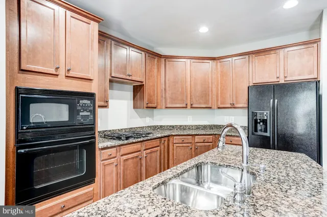 a kitchen with stainless steel appliances kitchen island granite countertop a stove a refrigerator and a sink with wooden cabinets