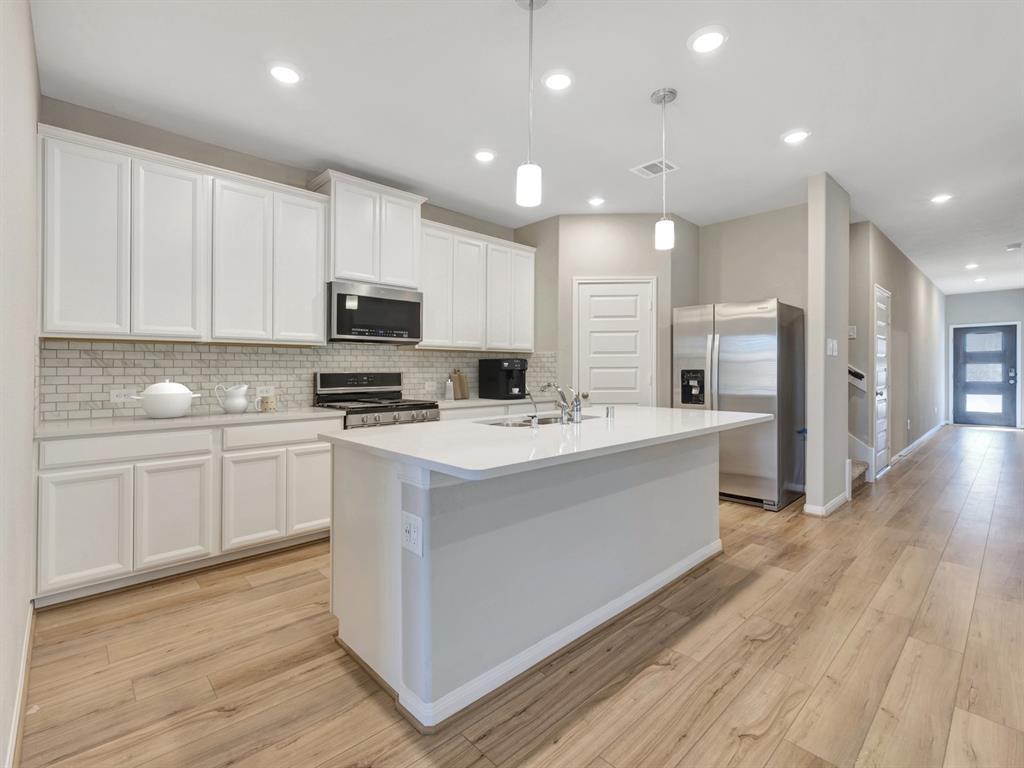 a kitchen with stainless steel appliances kitchen island granite countertop a stove top oven a sink a refrigerator and white cabinets with wooden floor