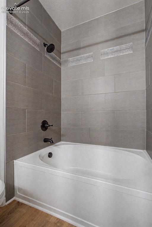 5353 Palomino Ranch Point, Unit 307 Colorado Springs, CO 80922 - Photo 27 of 30 Bathtub and shower combination featuring large format grey wall tiles with decorative accent bands, black showerhead, and black faucet fixtures