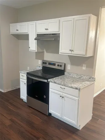 a kitchen with granite countertop white cabinets and a stove with wooden floor