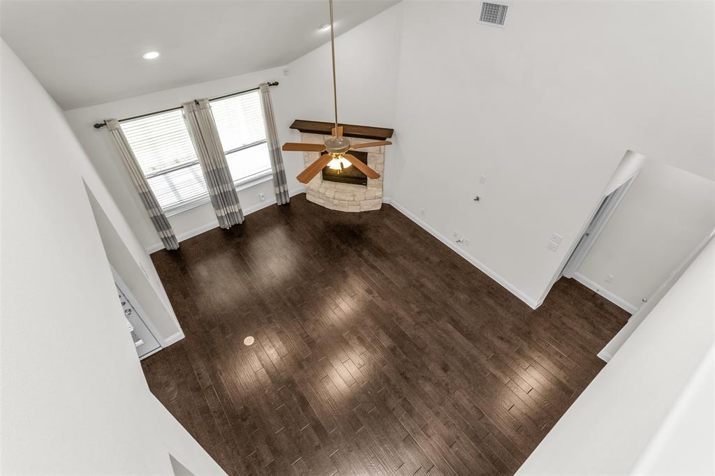 15713 Canyon Ridge Prosper, TX 75078 - Photo 33 of 38 Spacious room featuring vaulted ceilings, wood-finish flooring, a stone fireplace with a wood mantle, and a ceiling fan with integrated lighting