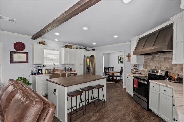 a kitchen with stainless steel appliances granite countertop a stove top oven a sink a dining table and chairs with wooden floor