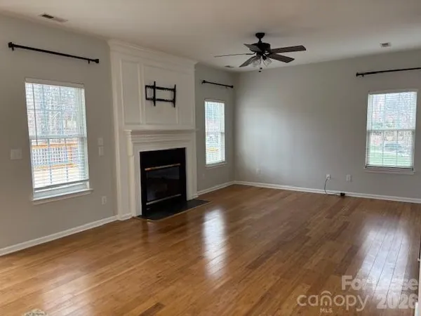 an empty room with wooden floor fireplace and windows