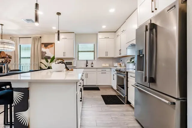 a kitchen with stainless steel appliances kitchen island granite countertop a refrigerator a sink and white cabinets
