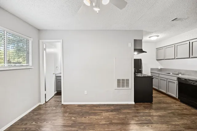 an empty room with wooden floor kitchen view and windows