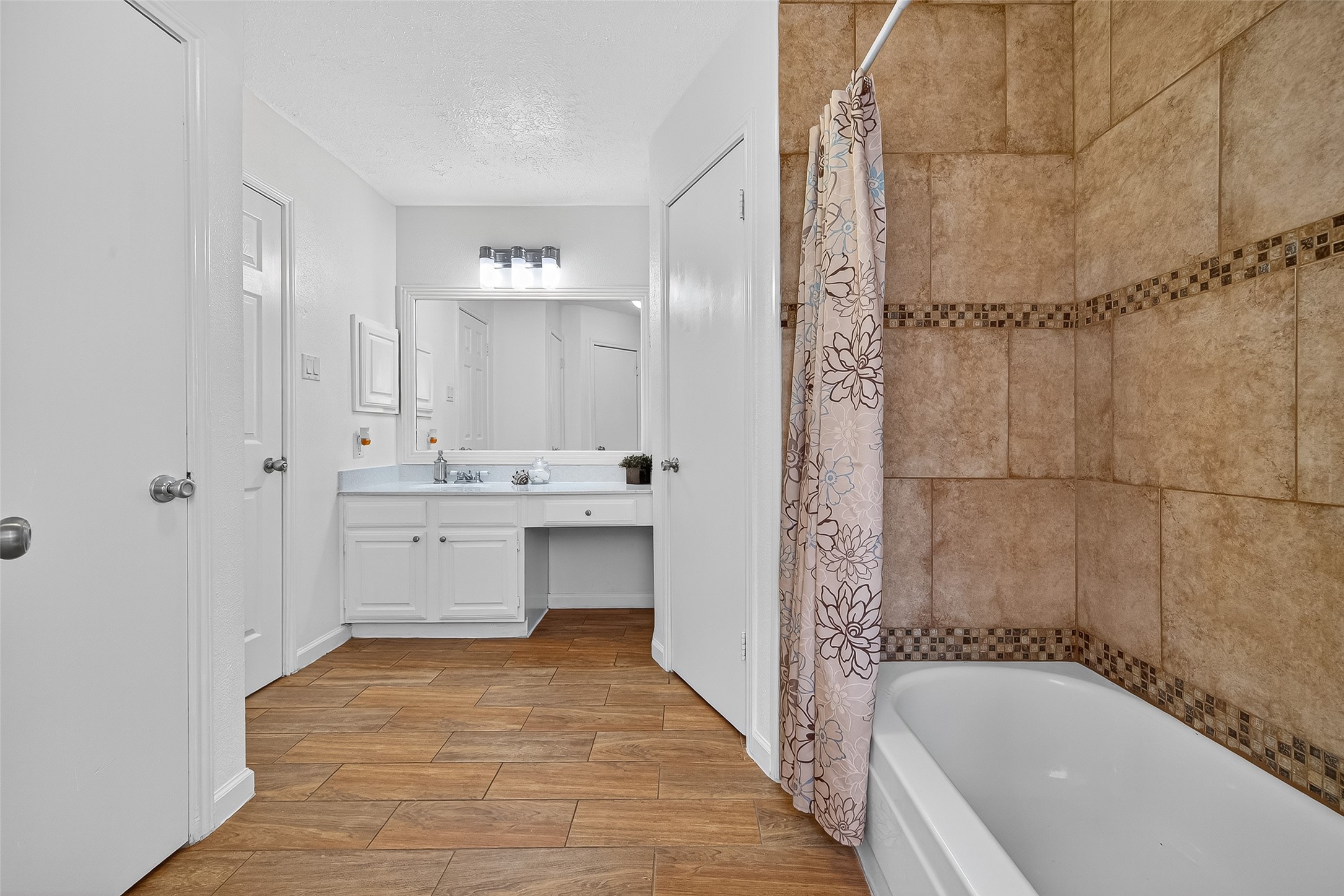 5323 Windsong Trail Houston, TX 77084 - Photo 18 of 30 This spacious primary bathroom offers access to his and hers closets and a tub/shower combo accented with decorative tile. The wood-look flooring ties the space together with a warm, cohesive design.
