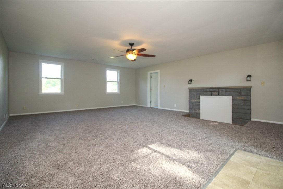 4113 Burgett Road Canfield, OH 44406 - Photo 4 of 31 Unfurnished living room featuring a stone fireplace, ceiling fan, and carpet flooring