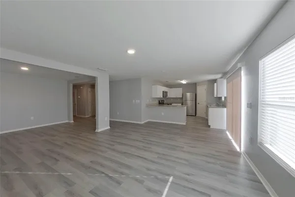 a view of empty room with wooden floor and kitchen