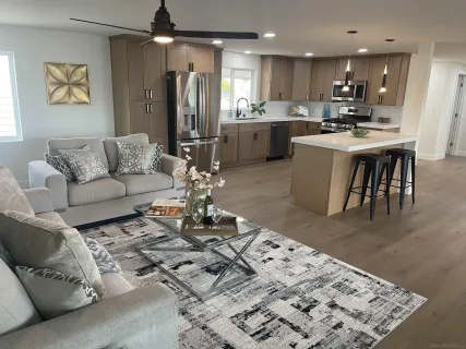 a living room with stainless steel appliances kitchen island granite countertop furniture a rug kitchen view and a chandelier