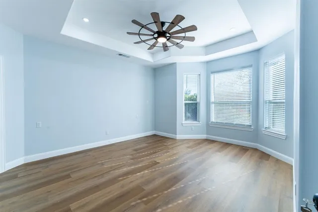 an empty room with wooden floor chandelier fan and windows