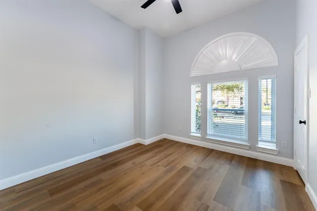 an empty room with wooden floor fan and windows