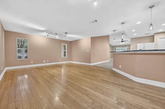 an empty room with wooden floor and kitchen view