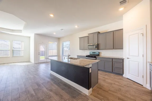 a large kitchen with stainless steel appliances granite countertop a stove a sink dishwasher and a refrigerator with wooden floor