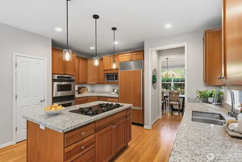 a kitchen with stainless steel appliances granite countertop a stove refrigerator and couches with wooden floor