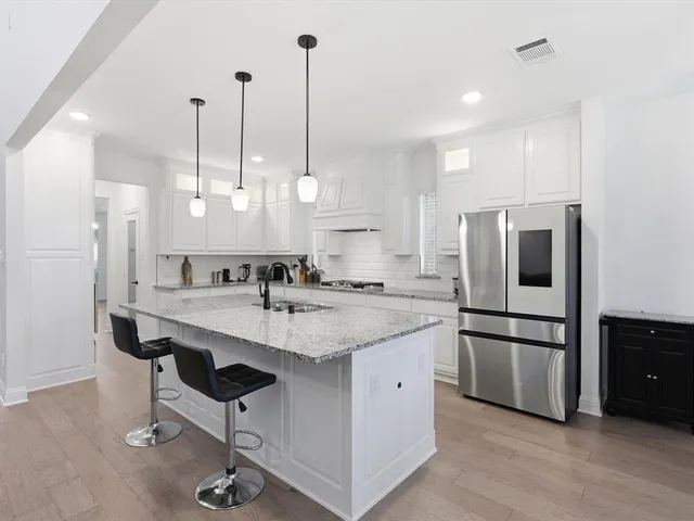 a kitchen with stainless steel appliances granite countertop a sink a stove a refrigerator and island with wooden floor