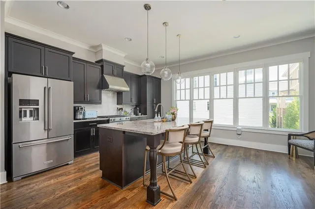 a kitchen with stainless steel appliances a dining table chairs stove refrigerator and wooden floor