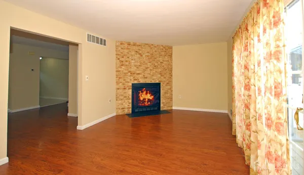 a view of an empty room with wooden floor and a fireplace