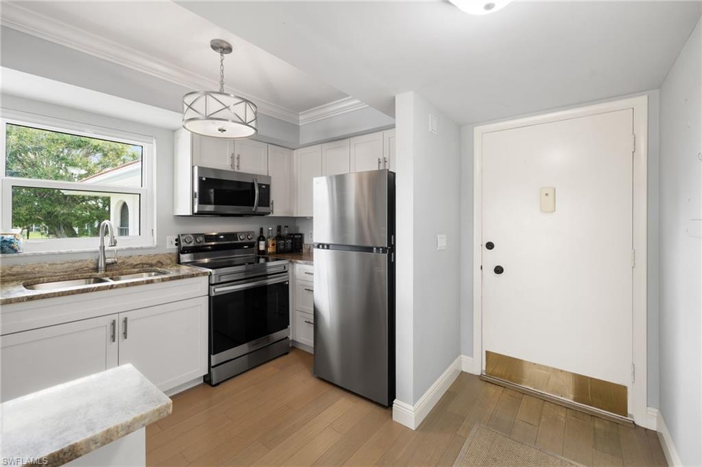 5 High Point Circle West, Unit 307 Naples, FL 34103 - Photo 6 of 31 a kitchen with stainless steel appliances granite countertop a refrigerator a stove a sink dishwasher a dining table and chairs with wooden floor
