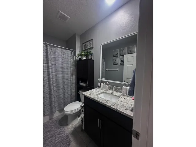 a bathroom with a granite countertop sink a toilet a mirror and shower