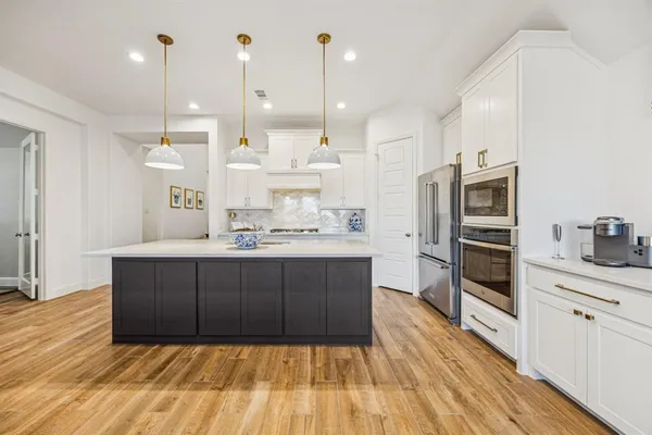 a kitchen with stainless steel appliances kitchen island granite countertop a refrigerator a oven and a wooden floors