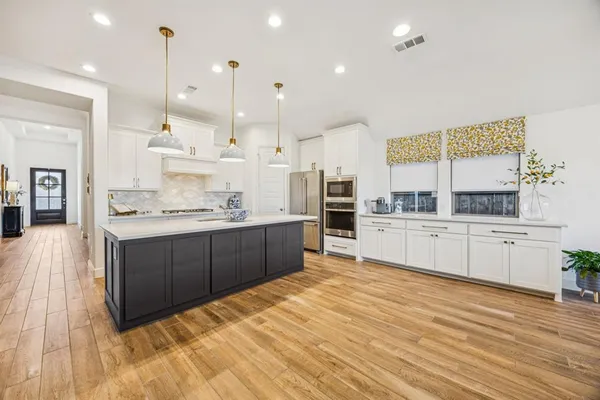 a large kitchen with stainless steel appliances kitchen island granite countertop a stove a sink and white cabinets