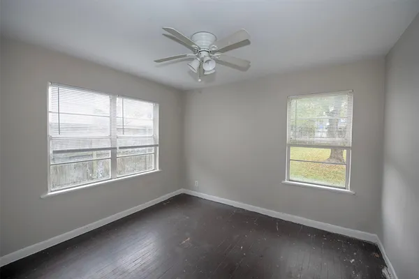 an empty room with wooden floor windows and fan