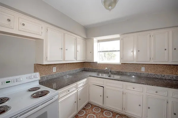 a kitchen with granite countertop white cabinets sink and stove