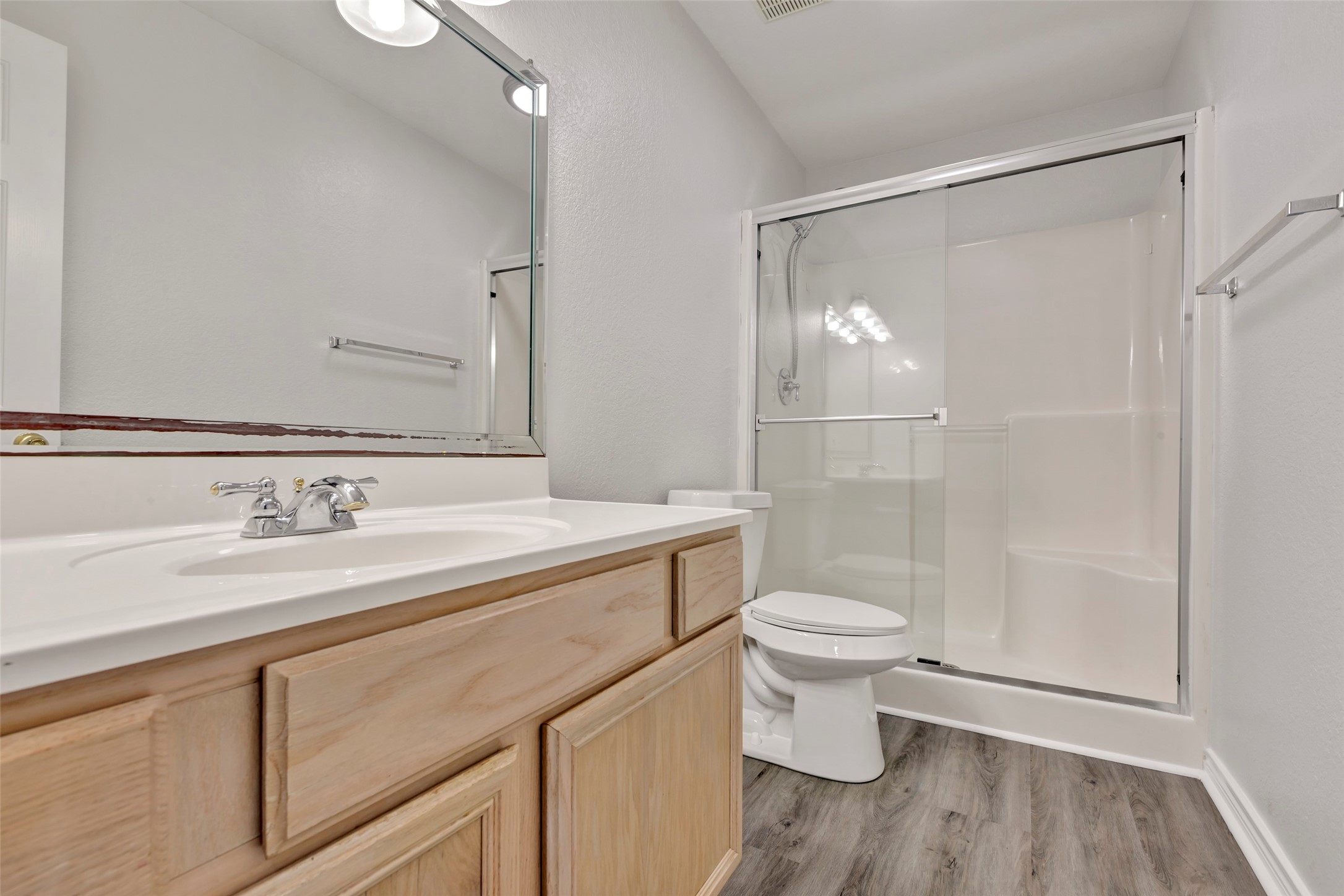 770 Hunt Road, Unit 212 Baytown, TX 77521 - Photo 35 of 40 This is a clean and modern bathroom with vinyl plank flooring, a large mirror over a single sink vanity, a toilet, and a full-size shower with sliding glass doors.