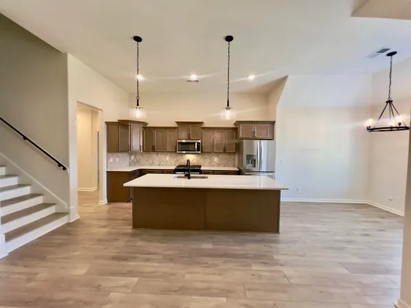 a view of kitchen with stainless steel appliances kitchen island granite countertop a stove a sink a refrigerator and a wooden floor