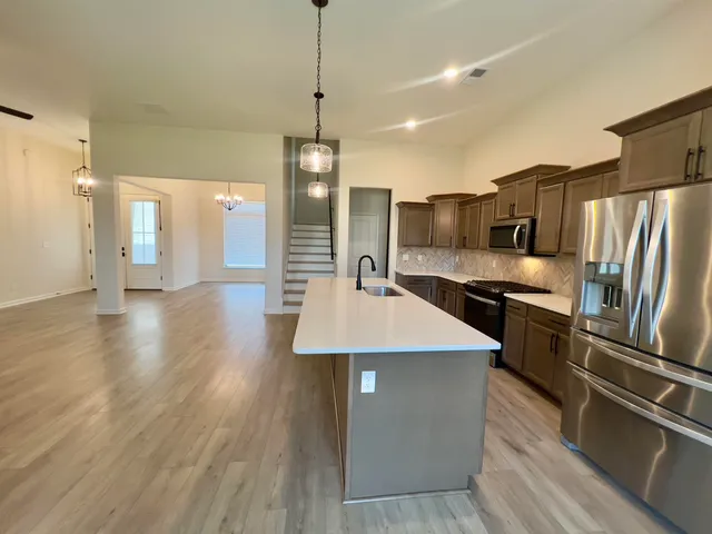 a kitchen with stainless steel appliances a refrigerator a sink dishwasher a stove and white cabinets with wooden floor